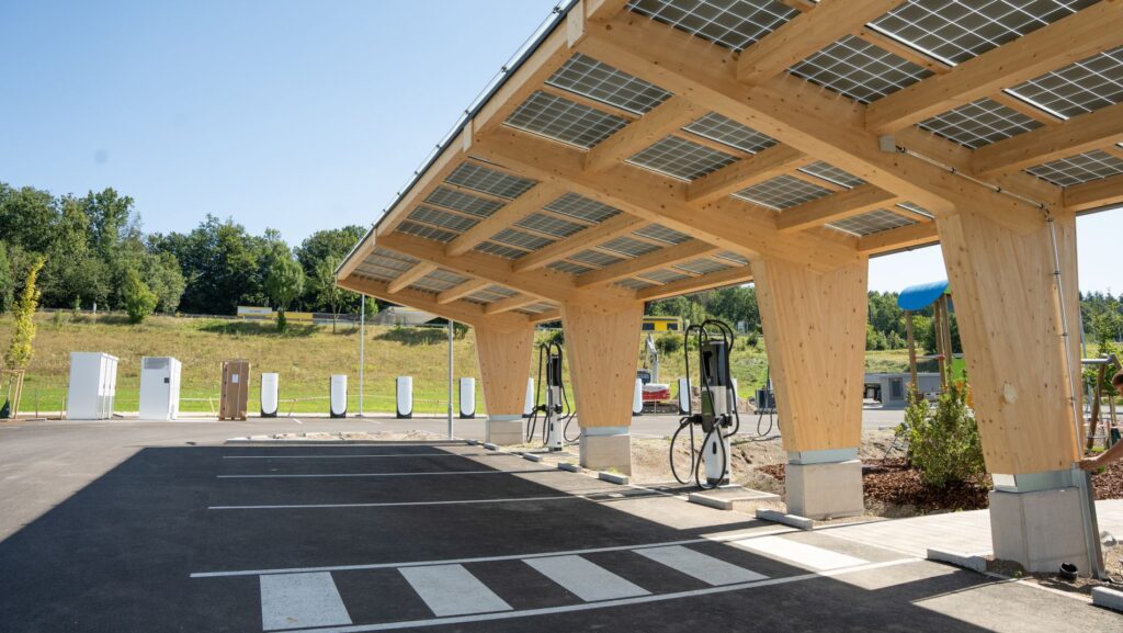 Moderner E-Ladepark in Amstetten mit Holzüberdachung und integrierten Solarpanelen auf dem Dach, ausgestattet mit mehreren Ladestationen.