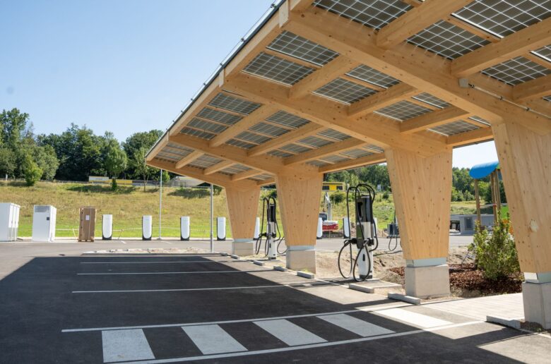 Moderner E-Ladepark in Amstetten mit Holzüberdachung und integrierten Solarpanelen auf dem Dach, ausgestattet mit mehreren Ladestationen.