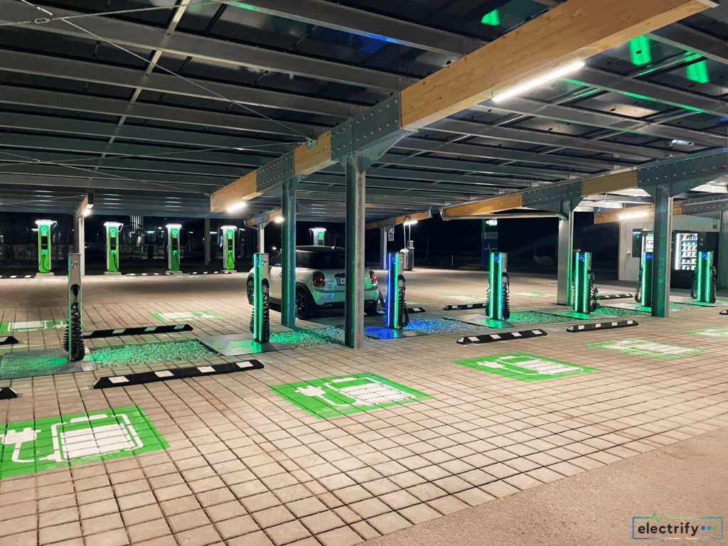 Innenansicht eines Solarcarports bei Nacht mit beleuchteten grünen Ladestationen und einem Elektroauto beim Laden.